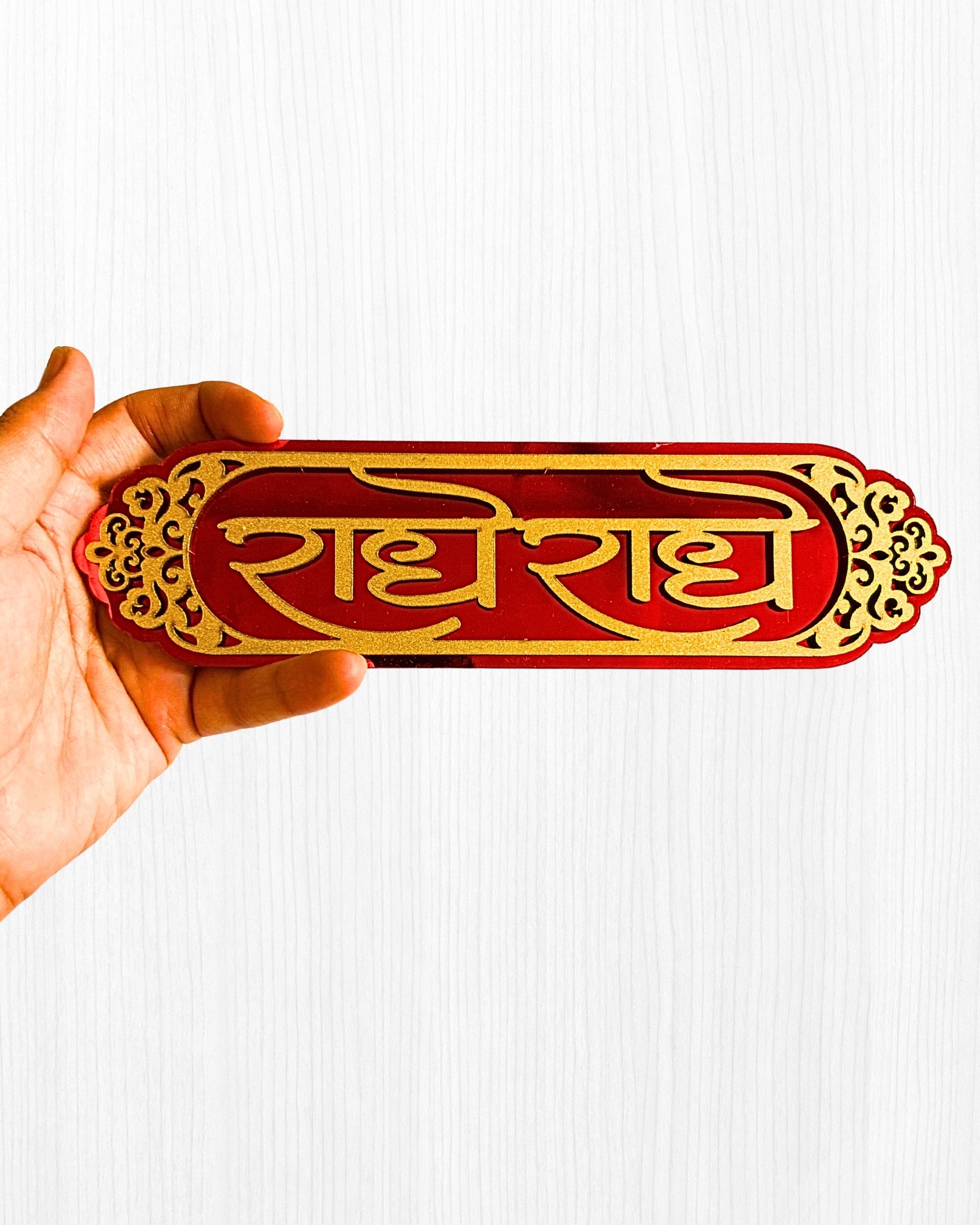 Close-up of a hand holding a red and gold decorative Chinese sign with ornate cut-out edges against a light background.