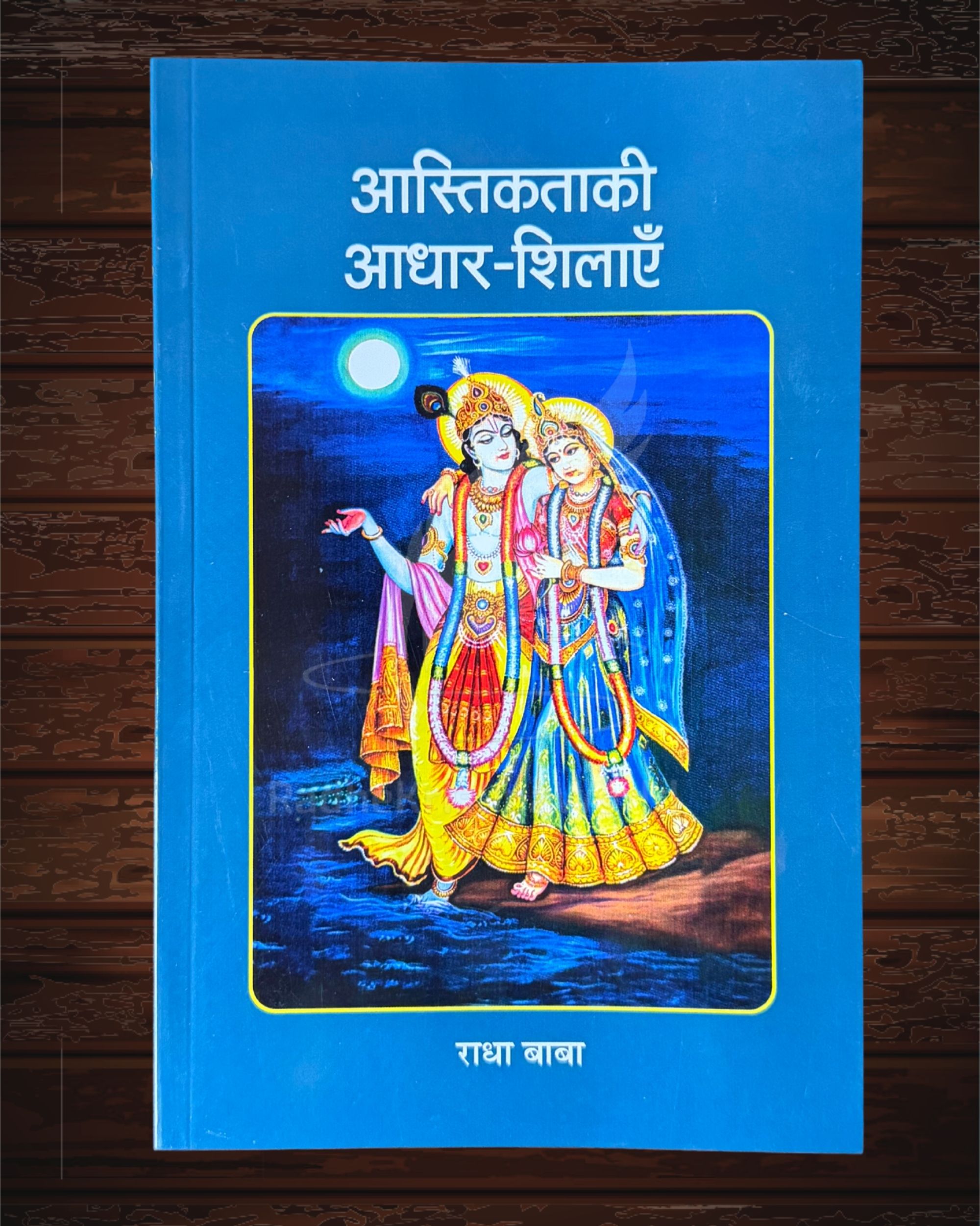 Blue book cover featuring a colorful Krishna and Radha illustration under a moonlit sky; Hindi title above the image.