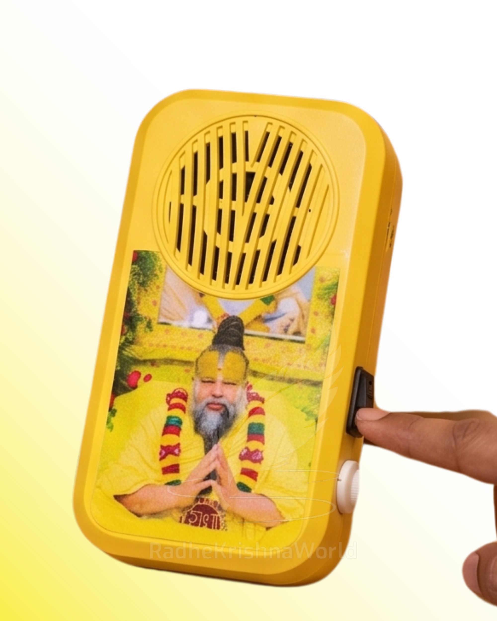 Close-up of a yellow handheld speaker/ran device with a circular vent and a devotional image on the front, with a hand on the side knob.