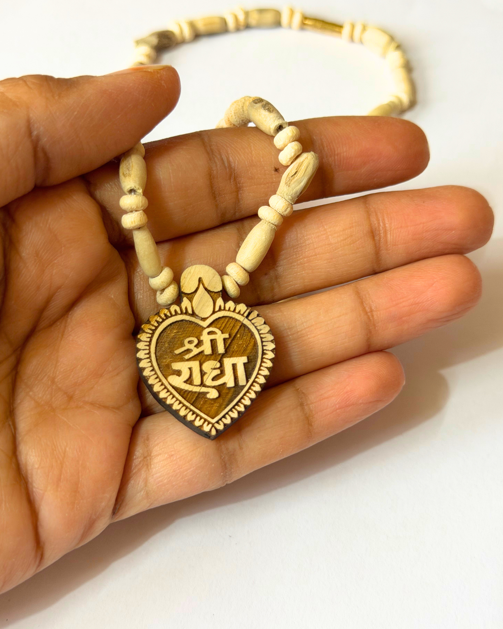 Close-up of a light wood bead bracelet held between fingers, showing a heart-shaped pendant with engraved text.