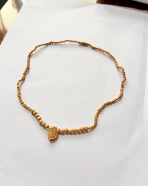 Beaded necklace with small tan beads and a carved circular pendant resting on white paper.