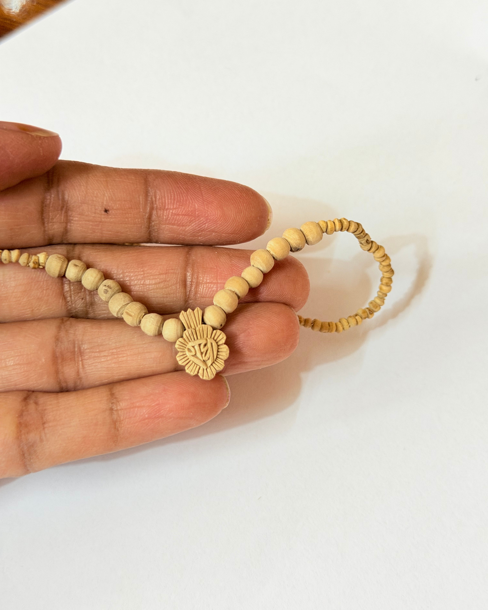 Close-up of a hand holding a string of small wooden beads with a carved floral pendant featuring an OM symbol in the center
