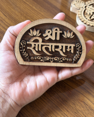 Close-up of a hand holding a round carved wooden medallion with an Om symbol and floral border on a wooden surface