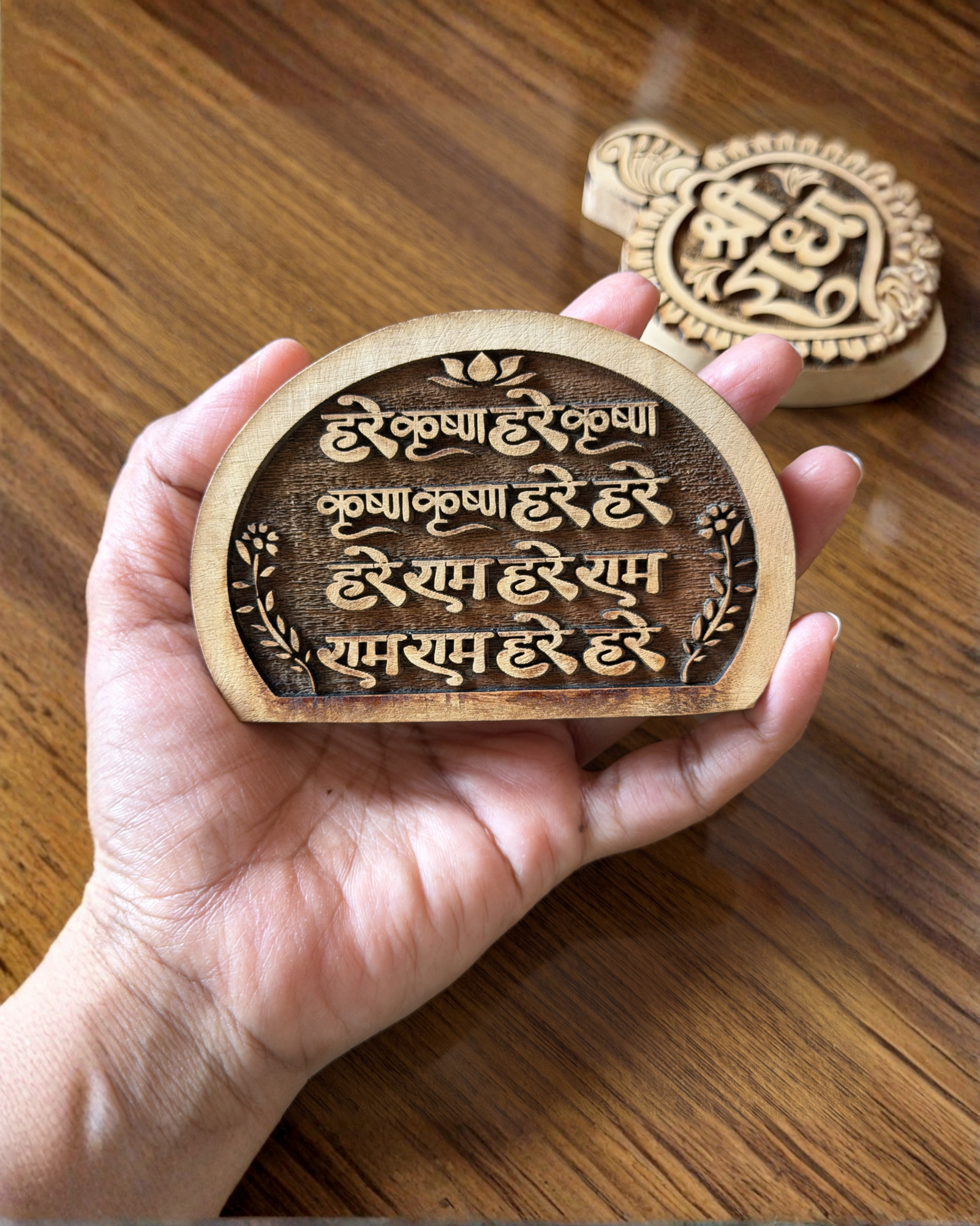 Close-up of a hand holding a round wooden medallion with Sanskrit script and a lotus motif.