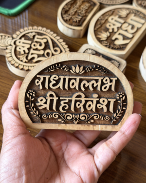 A hand holding a round wooden stamp with decorative Sanskrit/Hindi lettering and floral border, among other carved stamps on a table.