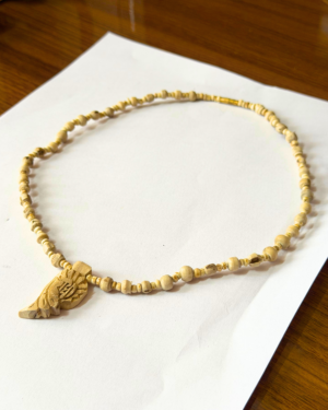 Cream-colored beaded necklace with a large carved pendant laid on white paper on a wooden table edge.