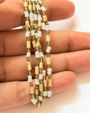 Close-up of multiple gold and white beaded bracelets held between fingers.