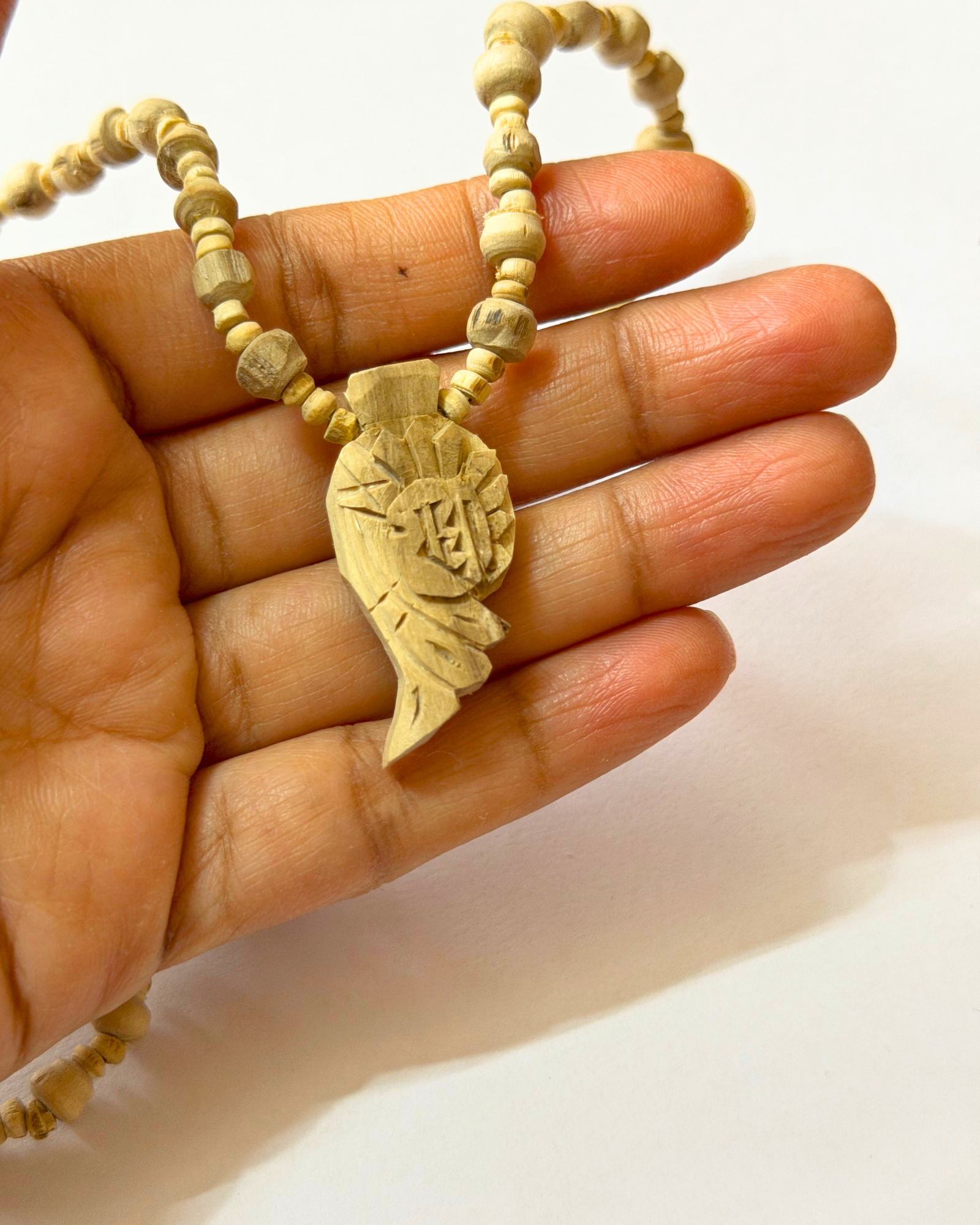 Wooden beaded necklace held between fingers with a carved pendant visible on the cord.