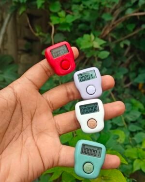 Five small digital counters in red, gray, white, turquoise, and mint held on a hand against green foliage.