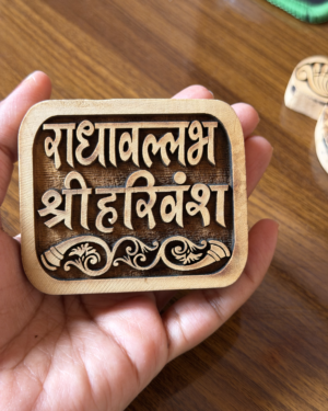 Close-up of a wooden carved stamp held in a hand, featuring Hindi lettering and decorative scrollwork.